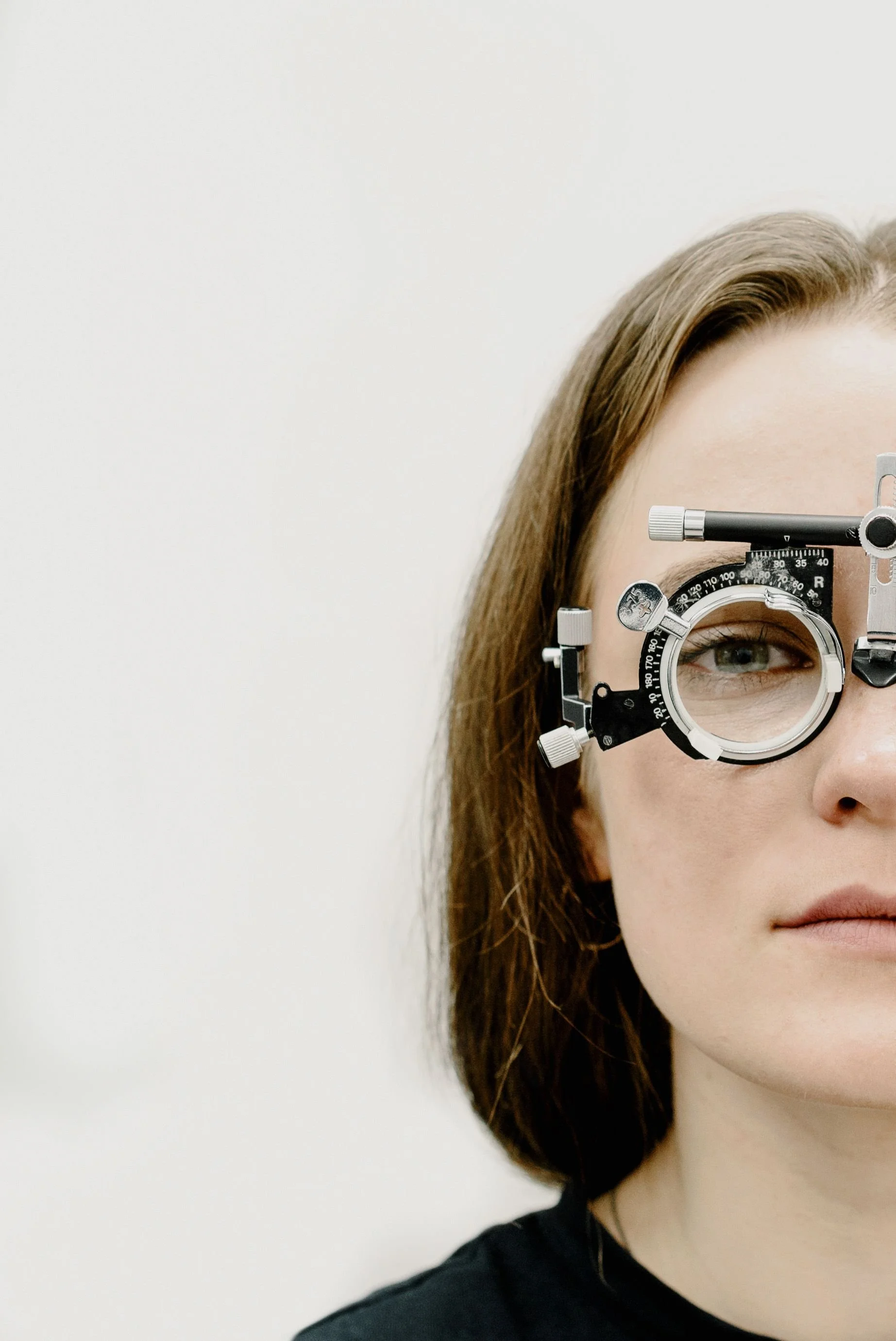 Close-up of a woman with brown hair wearing an optometry trial frame against a white background.
