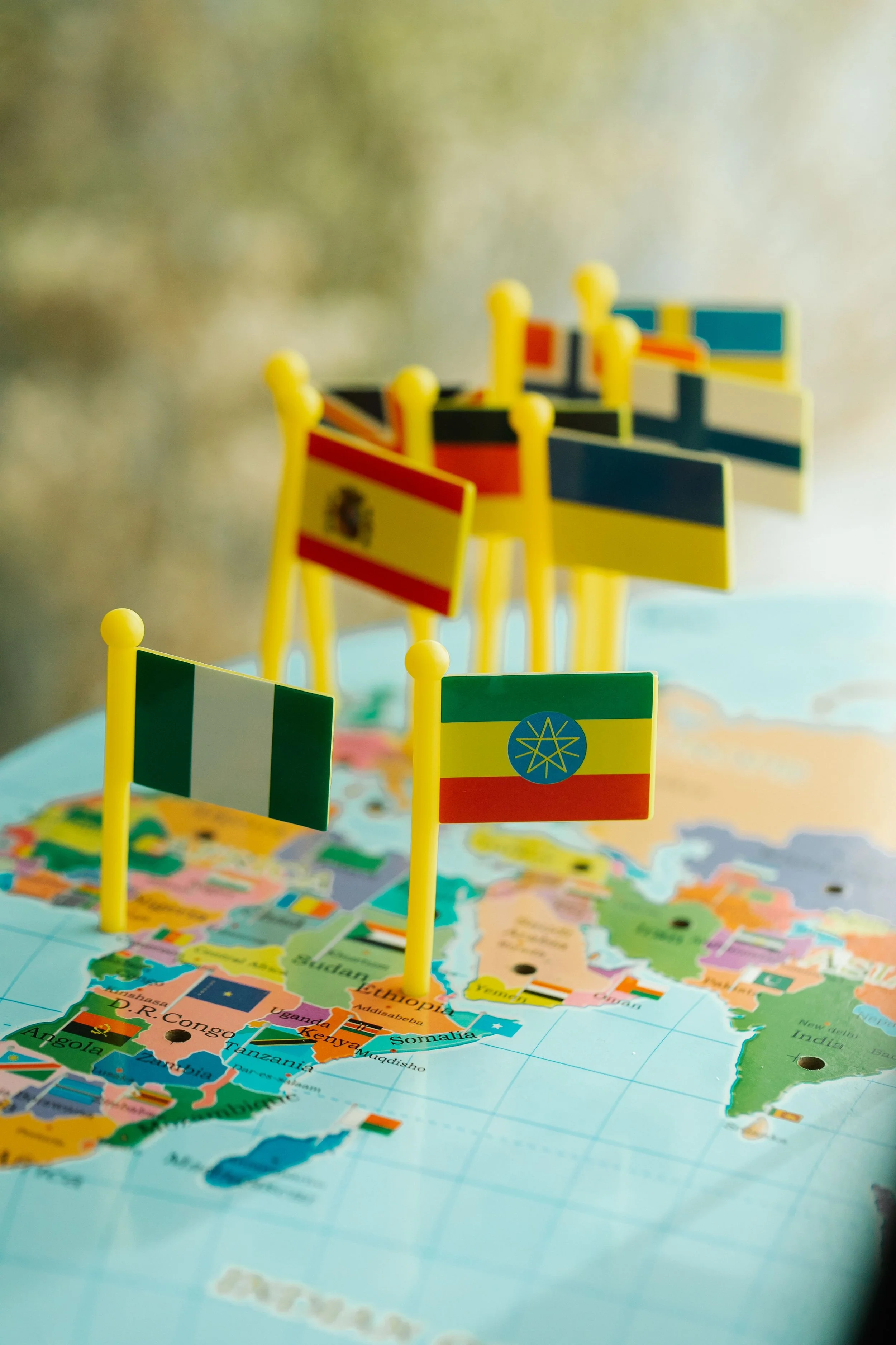 Colorful miniature flags of various countries placed on a world map showing Africa, with some of the flags visible, including Spain, Ethiopia, and Kenya.