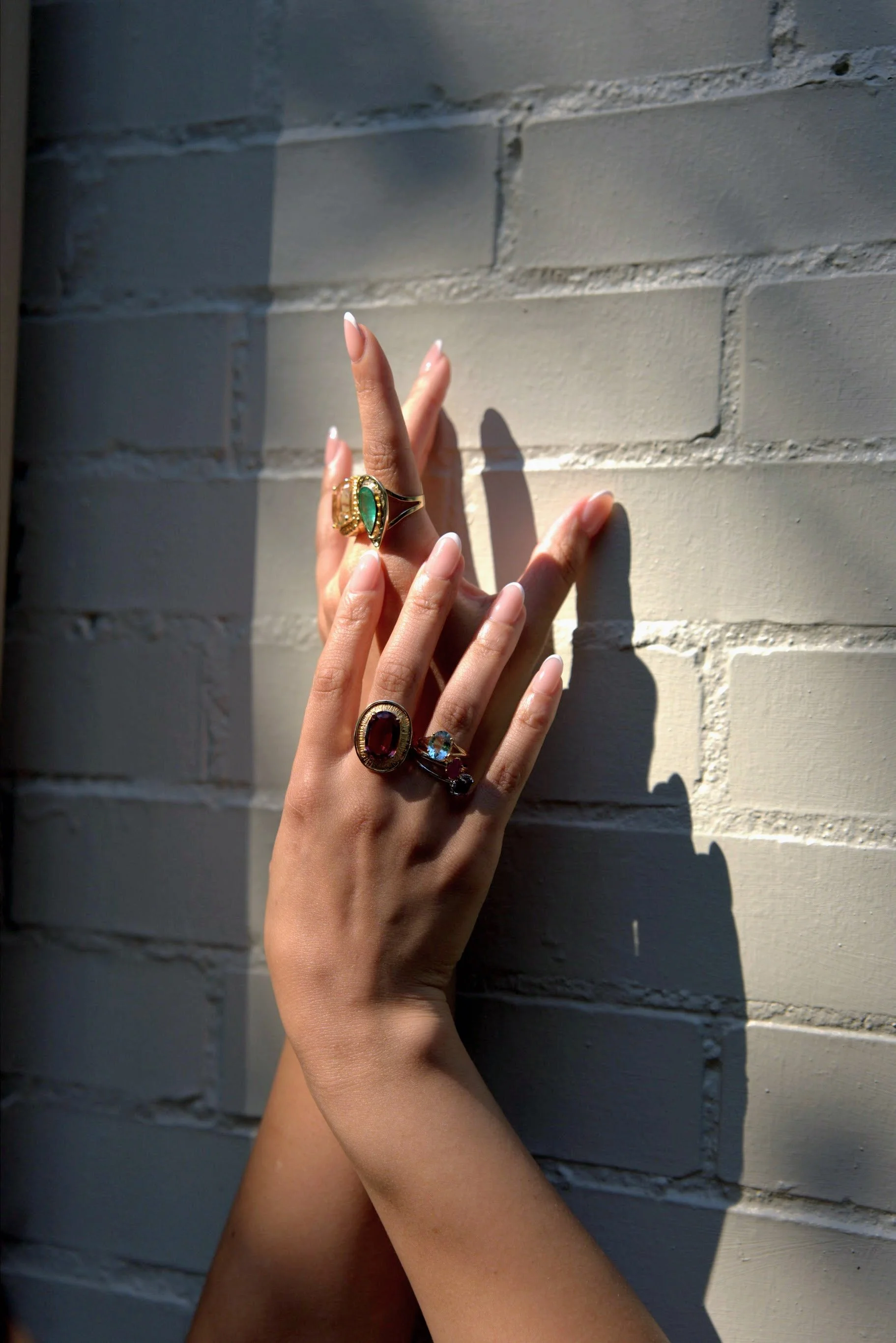 A person's hands with multiple rings, touching a white brick wall, casting shadows.