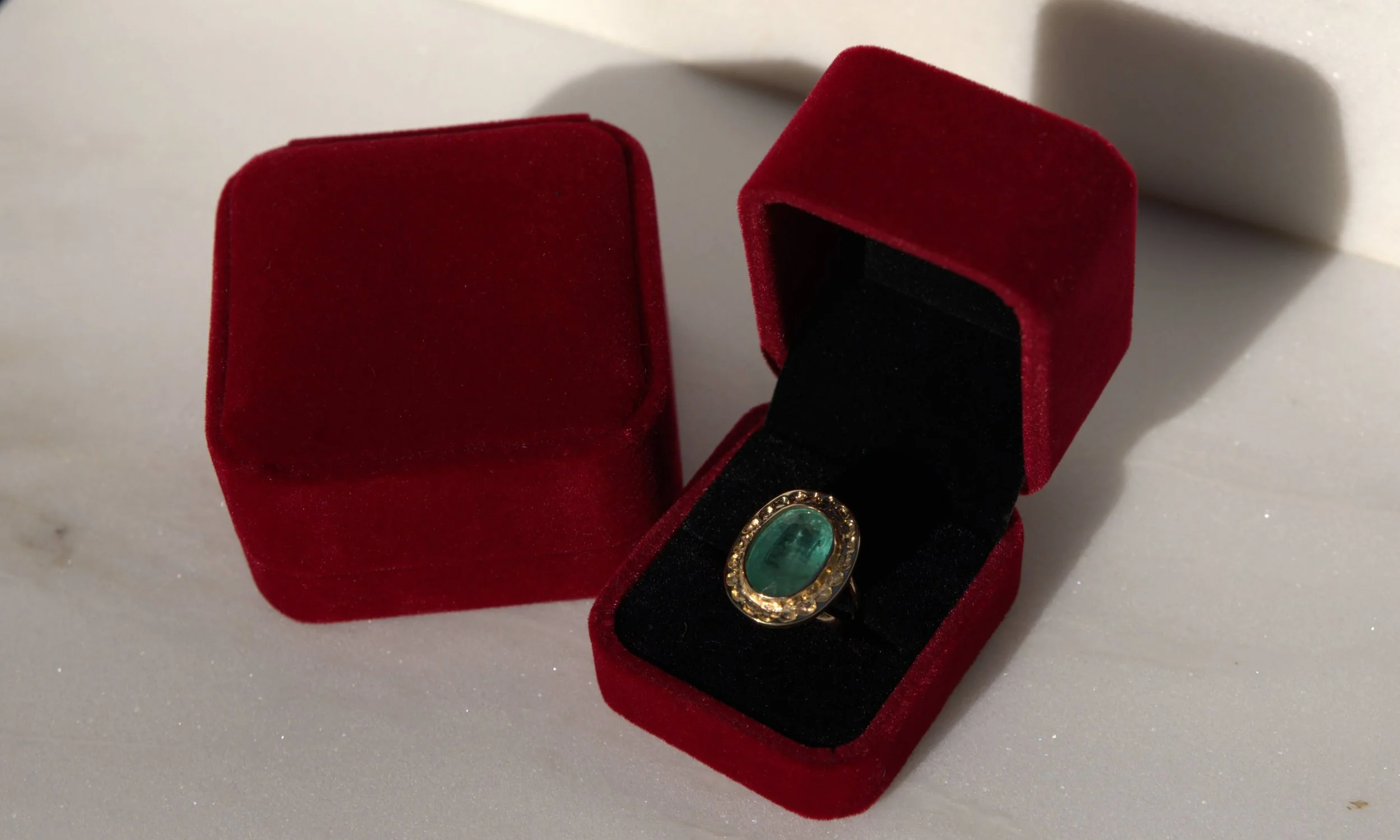 A red velvet ring box with a black interior, holding an oval-shaped turquoise gemstone ring decorated with small diamonds, placed on a white surface.