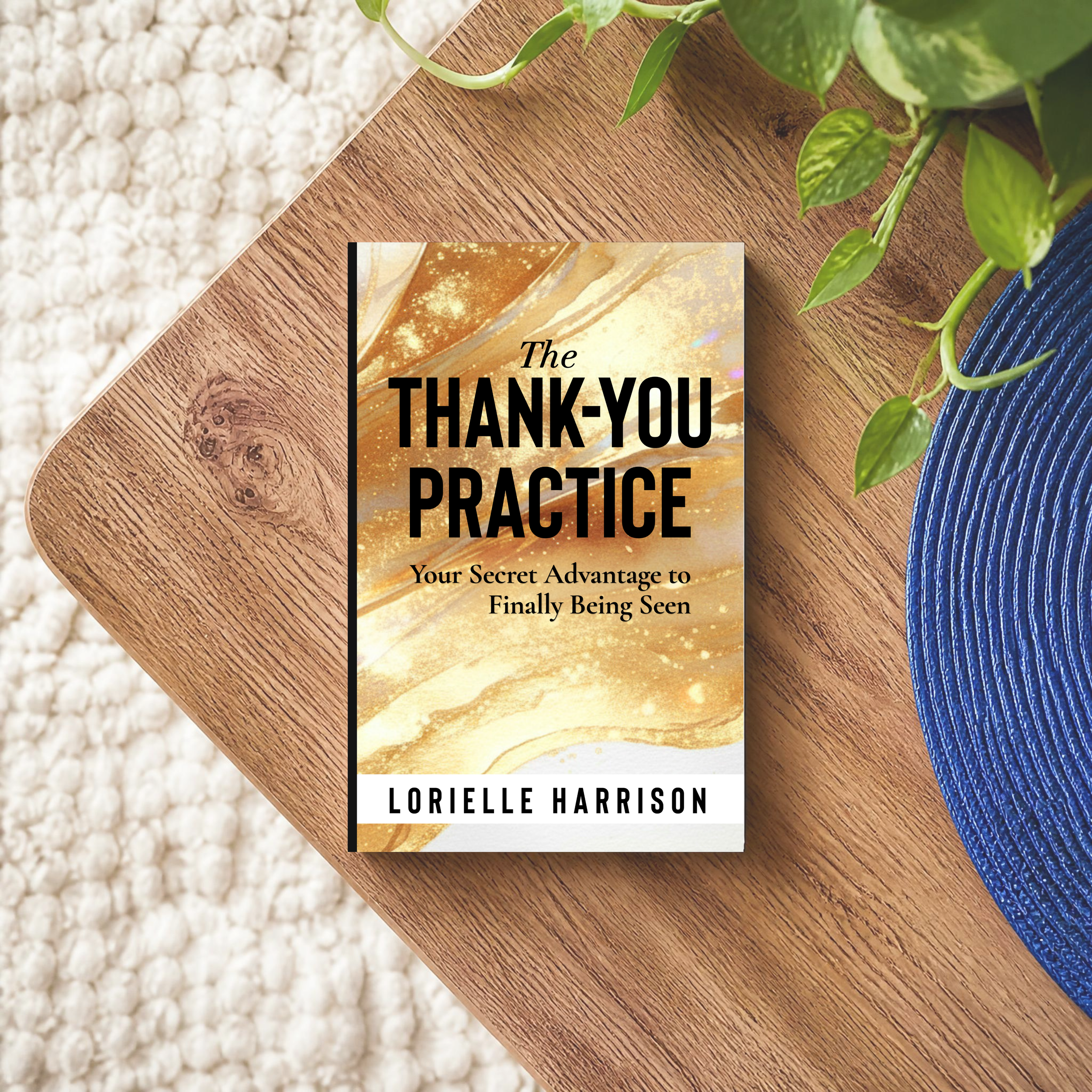Close-up of the self-help book titled 'The Thank-You Practice' by Lorielle Harrison, placed on a round wooden surface with green houseplants, with a textured cream-colored rug in the background.