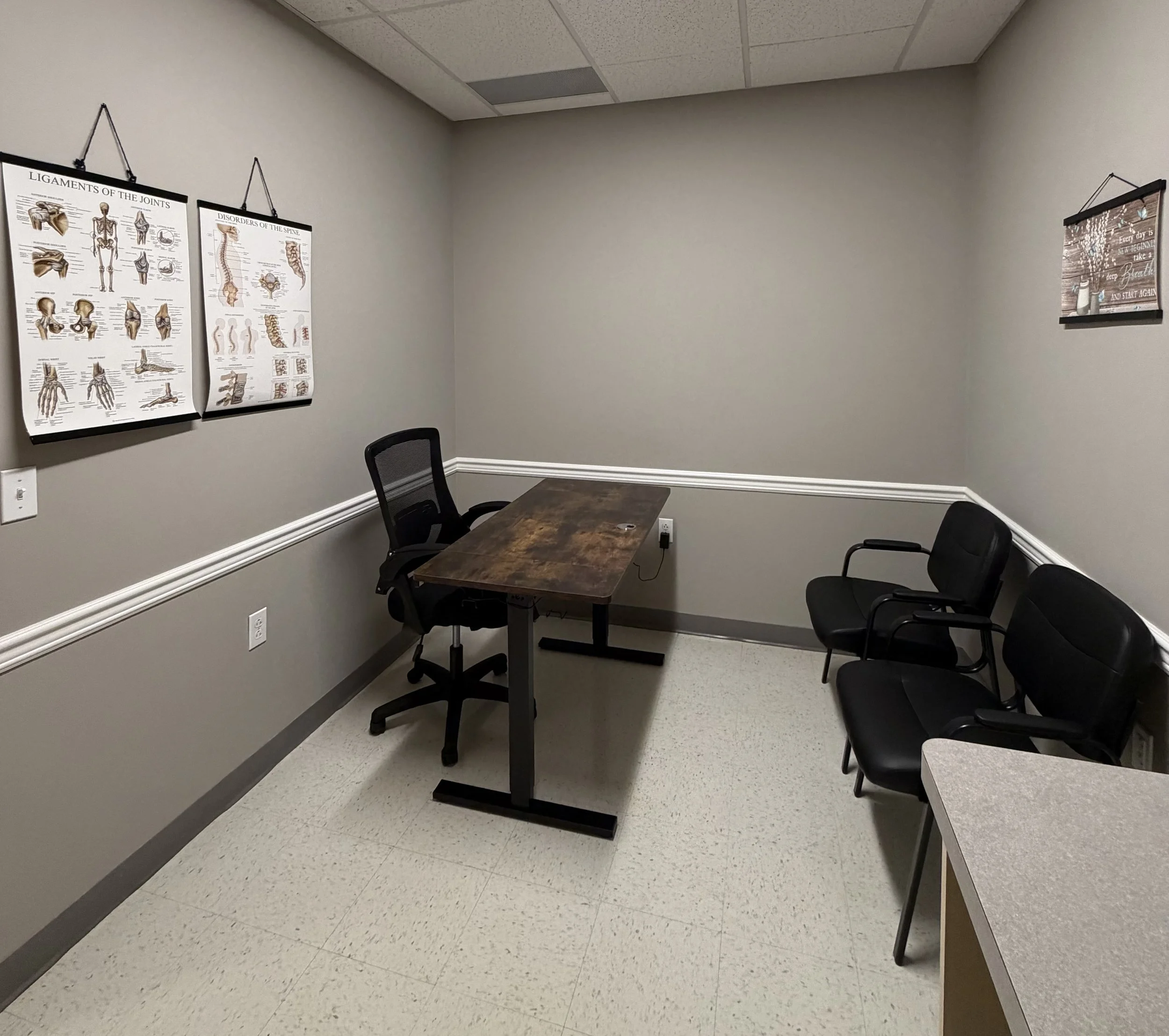 Compassionate Pain Care and Wellness Exam room with two black chairs and one brown desk and black rolling chair