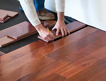 Person installing hardwood flooring, measuring and marking the wood planks.