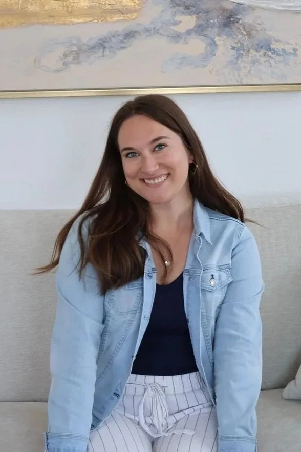 Annalise Maull, LMFT sitting on a beige sofa and smiling at the camera. There is a light-colored wall and abstract artwork in the background.