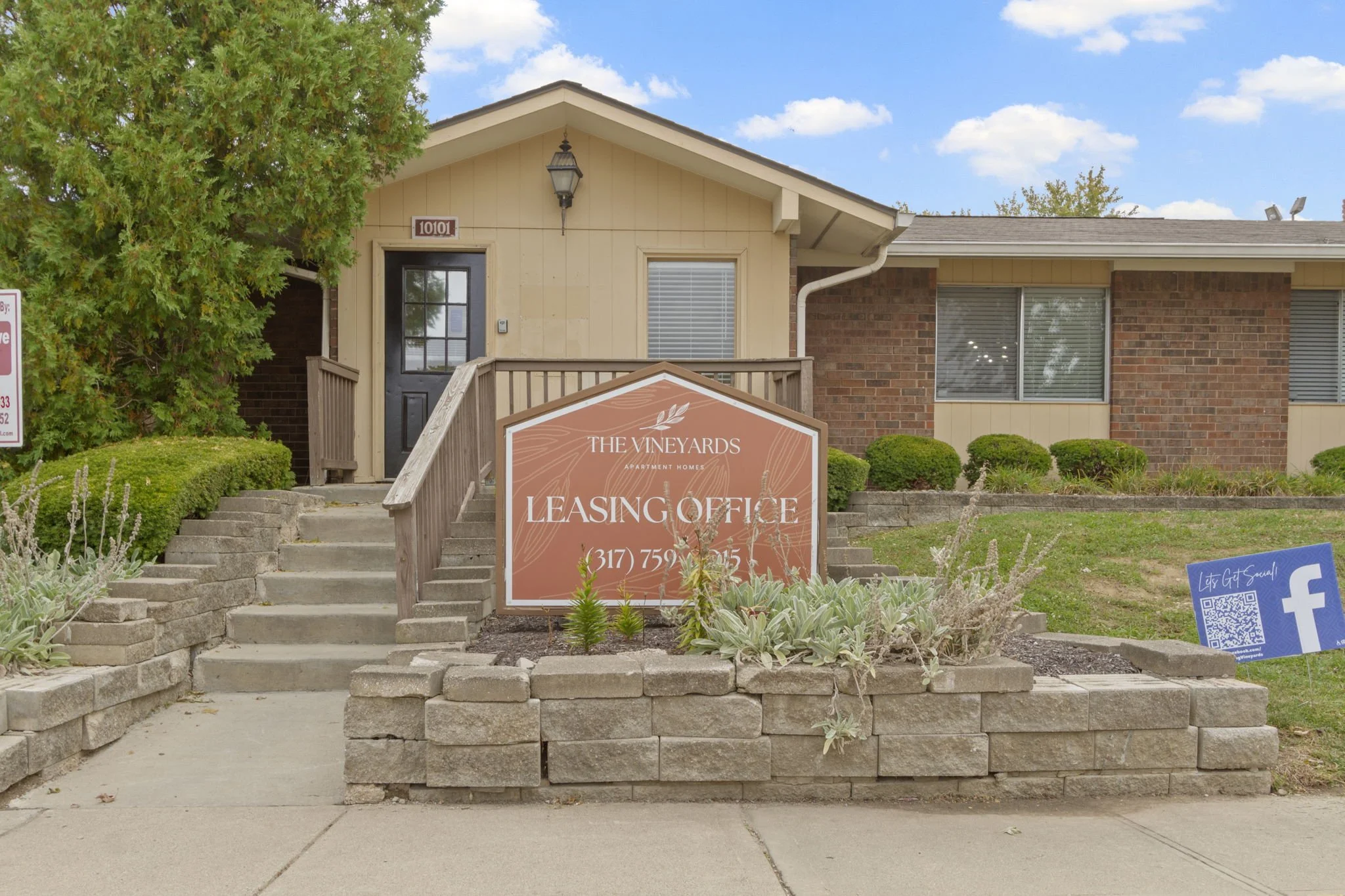 Residential building with a sign indicating leasing office for The Vineyards Apartment Homes, located at 10101, with a staircase leading to the front door and landscaped bushes in front.