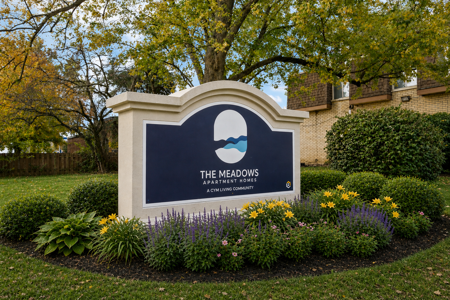 Sign for The Meadows apartment community surrounded by green bushes and flowers, with trees and a building in the background.