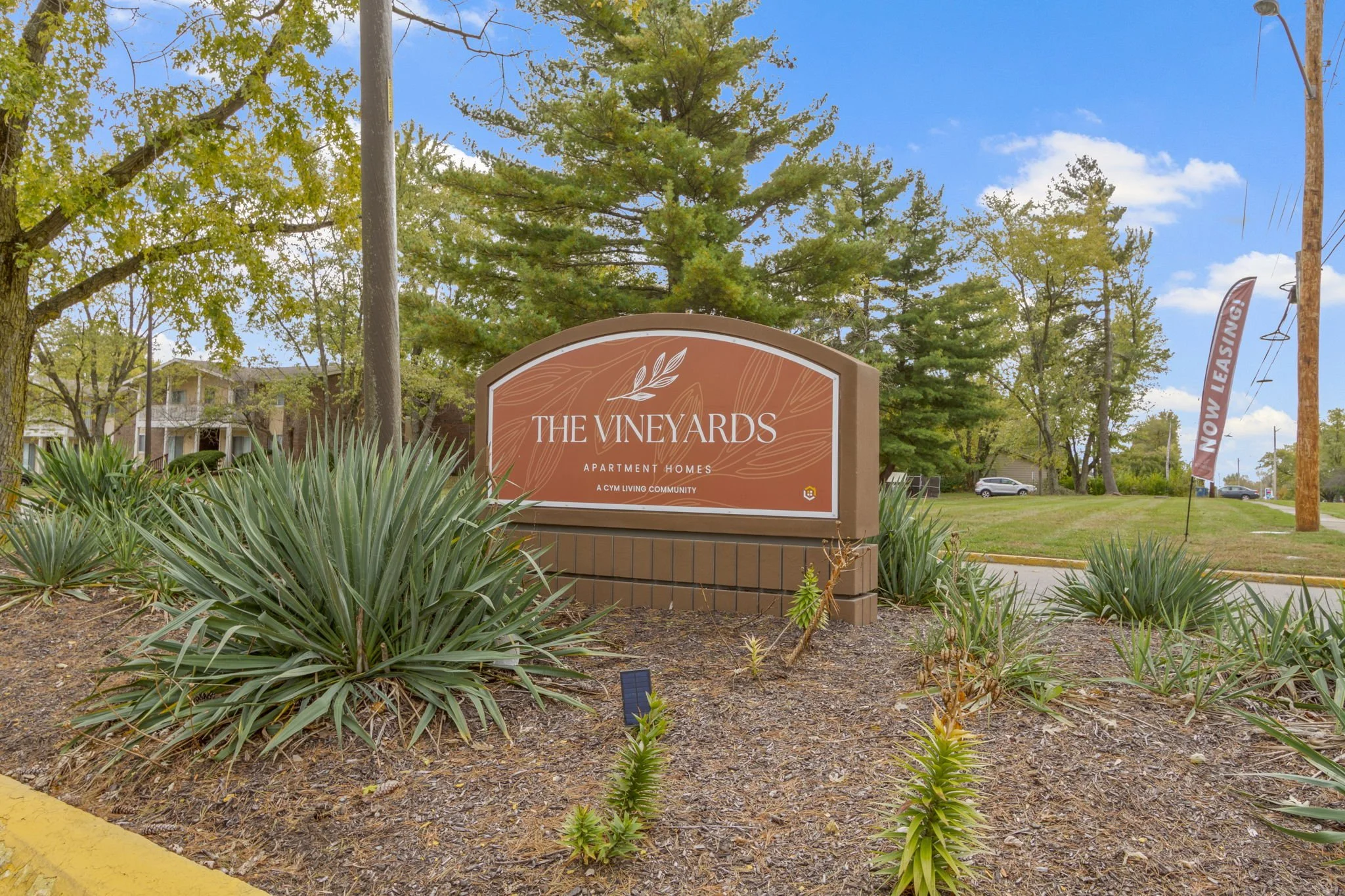 Sign for The Vineyards apartment homes in a landscaped area with plants, trees, and a clear blue sky.