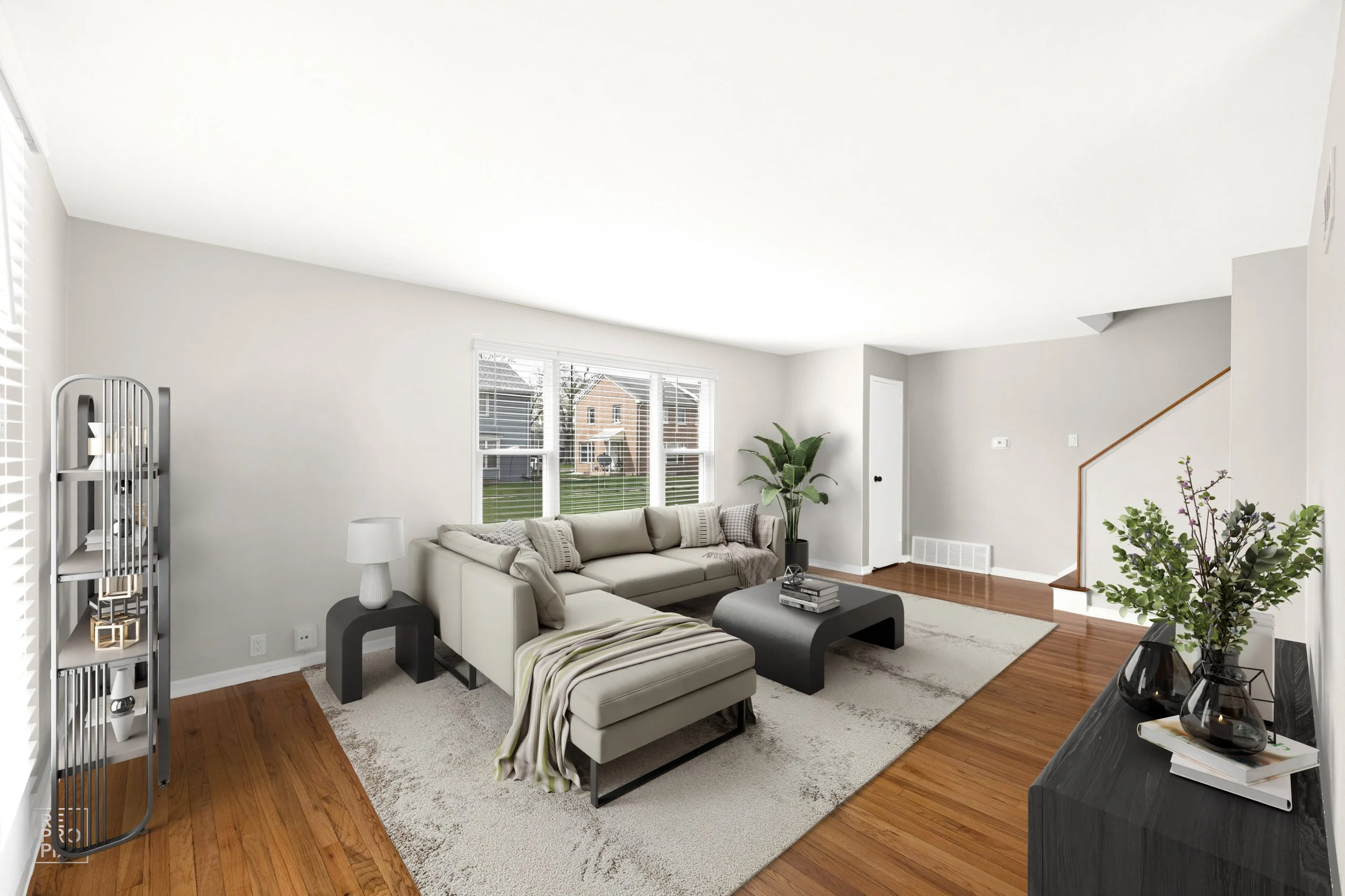 Living room with a beige sectional sofa, black coffee table, gray side table with a white lamp, large windows with white blinds, house plants, and hardwood floors.