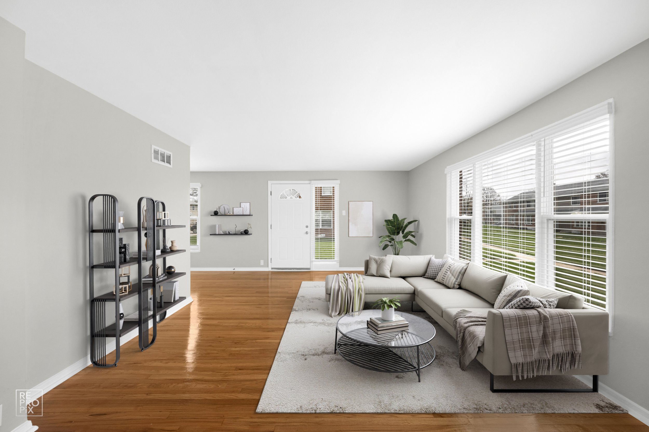 Bright living room with large windows, white sofa, black metal coffee table, beige rug, plants, and wall decor, hardwood floor, white walls.