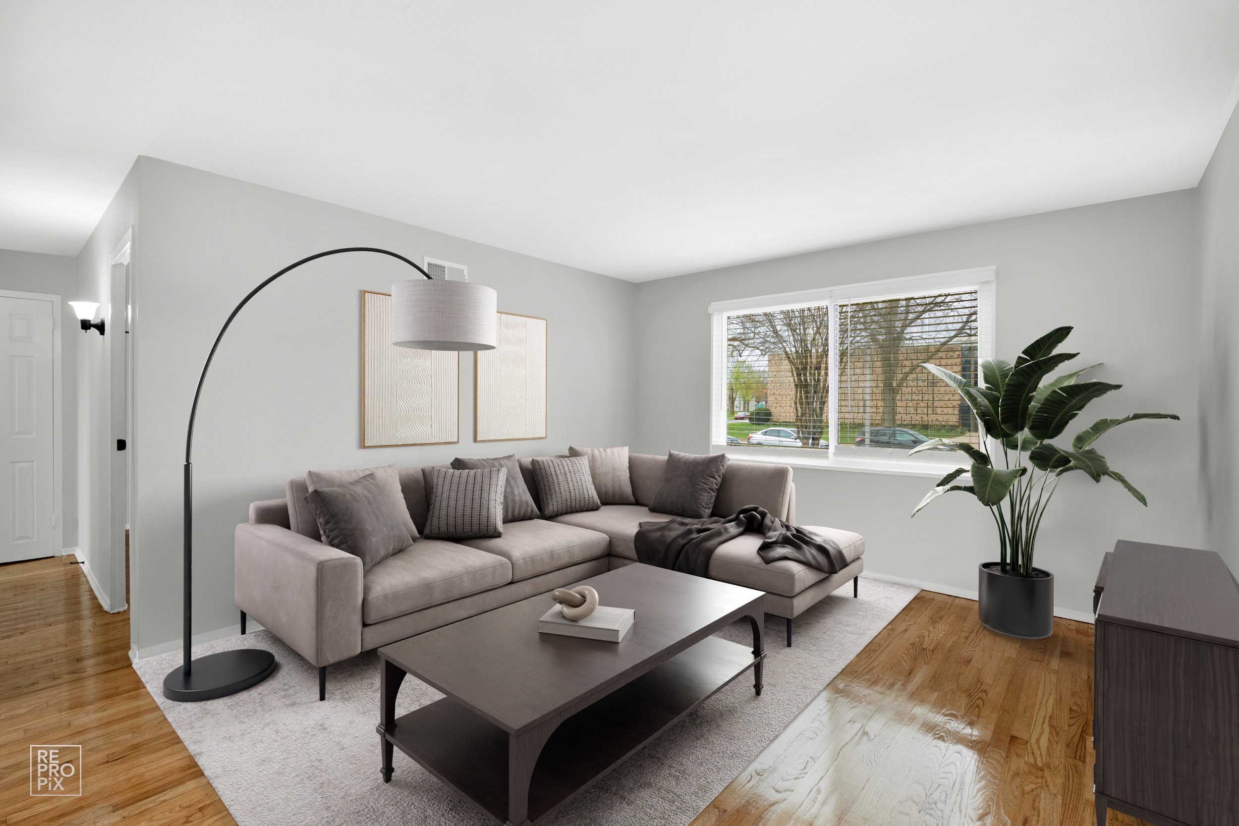 Living room with a large beige sectional sofa, a dark gray coffee table, a green potted plant, large window, and light gray walls.