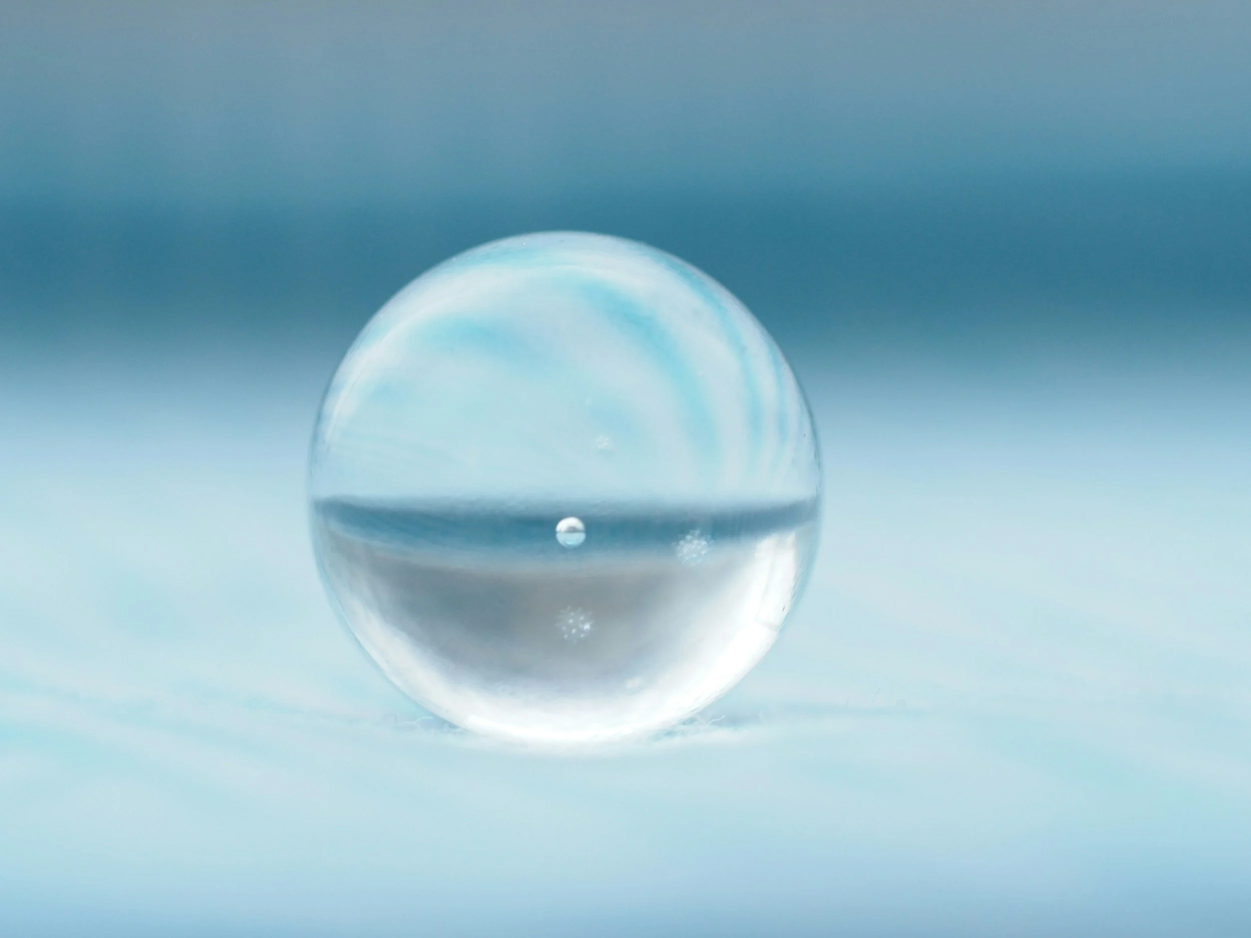 A clear glass marble or sphere on a light blue surface with a blurred gradient blue background.