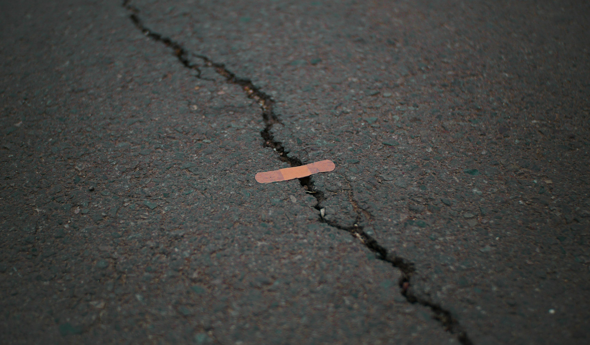 A close-up of a cracked asphalt road with a band-aid placed along the crack.