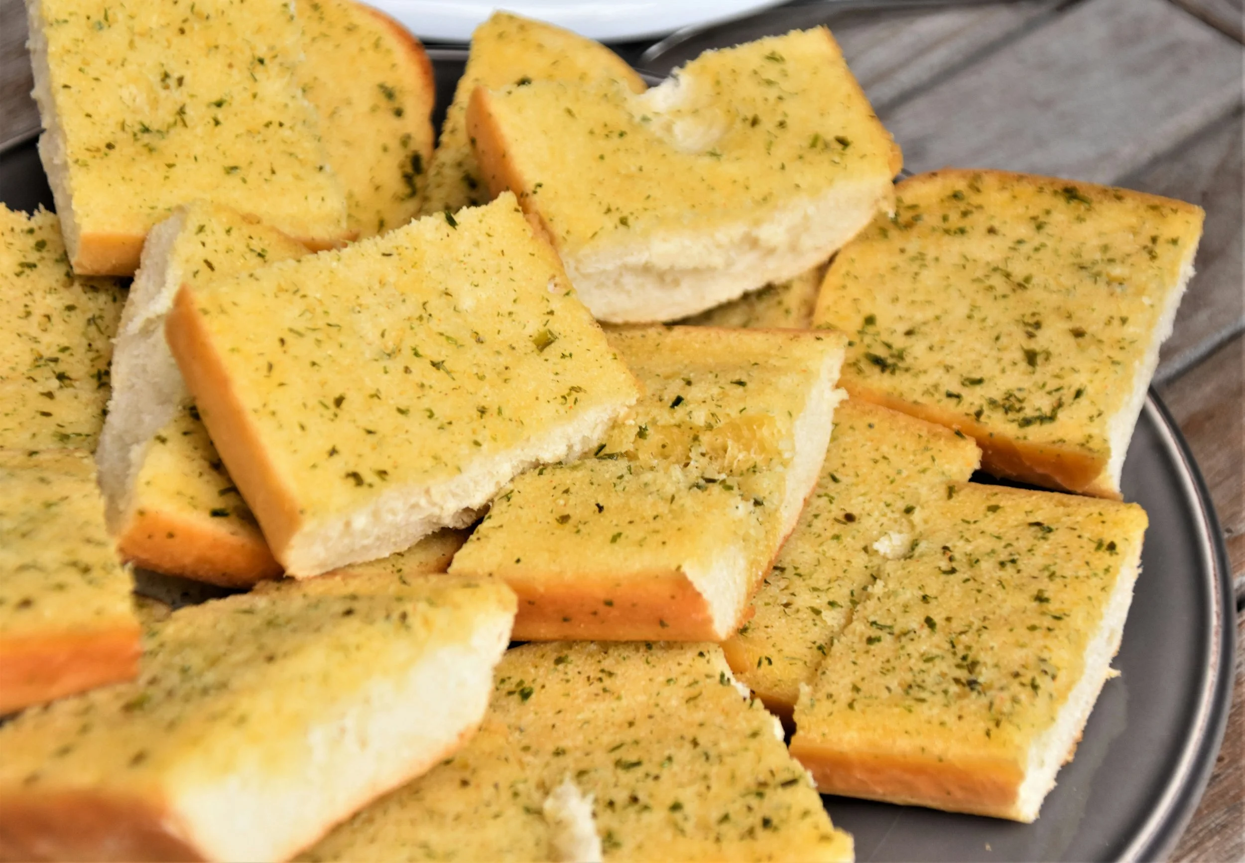 Close-up of garlic bread slices seasoned with herbs on a black plate