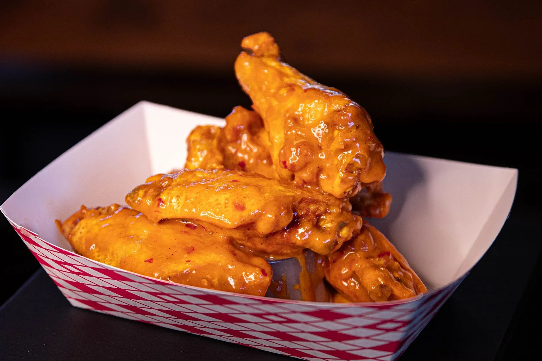 Three pieces of buffalo chicken wings covered in orange sauce inside a red and white checkered food tray