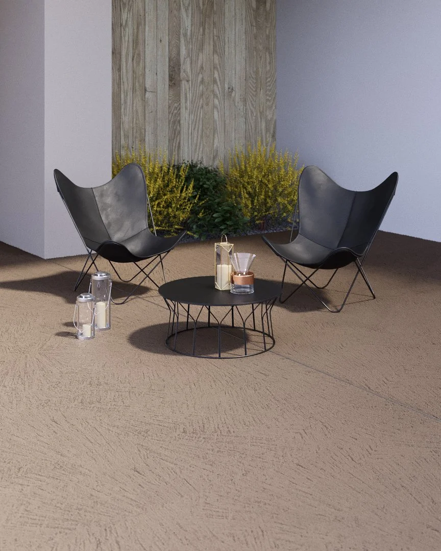 Two black modern lounge chairs with curved backs facing inward, a round black coffee table in between, with candles and decor items on it, in a room with beige carpet, a white wall, and a decorative wooden panel with yellow and green plants behind.