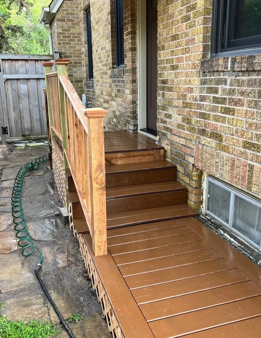 Newly constructed wooden front steps and porch with a railing leading to a house with brick exterior walls and a glass door.