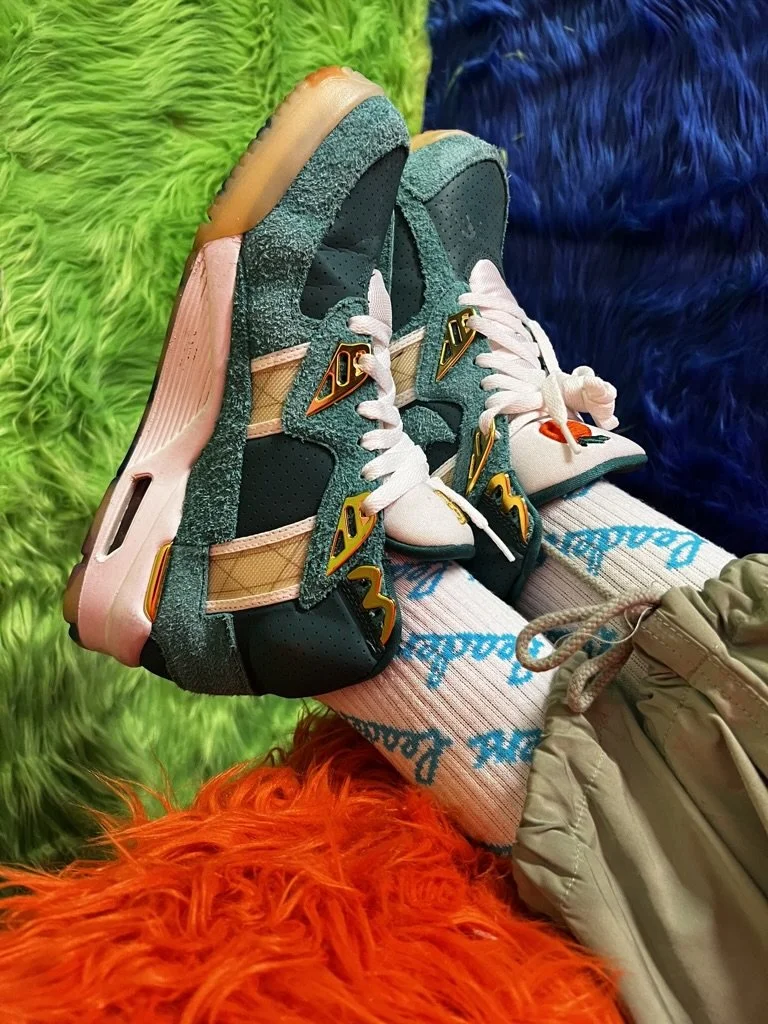 A pair of colorful sneakers resting on a person's lap, surrounded by bright green, orange, red, and blue furry blankets.