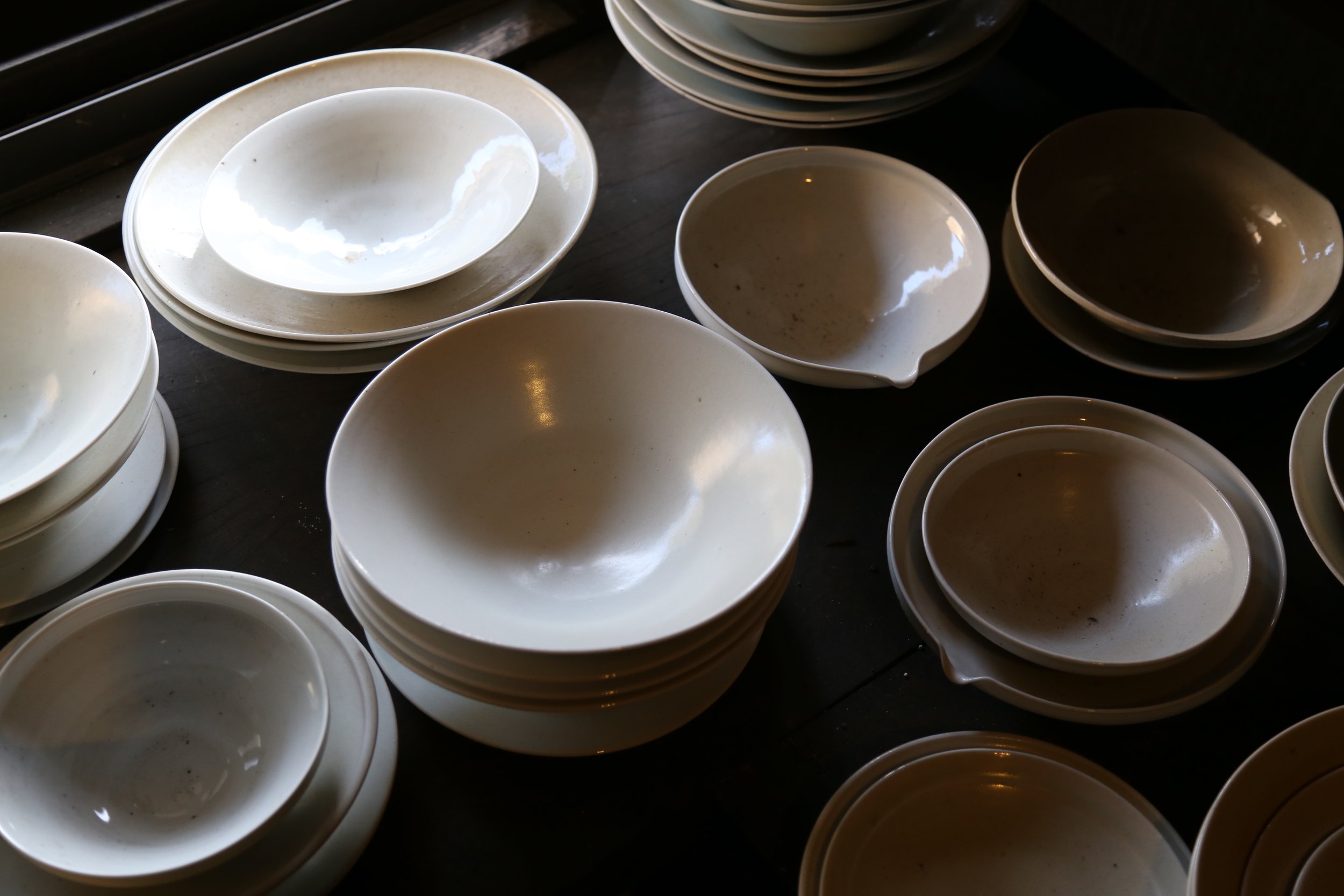 Stacked white ceramic bowls and plates on a dark wooden surface.