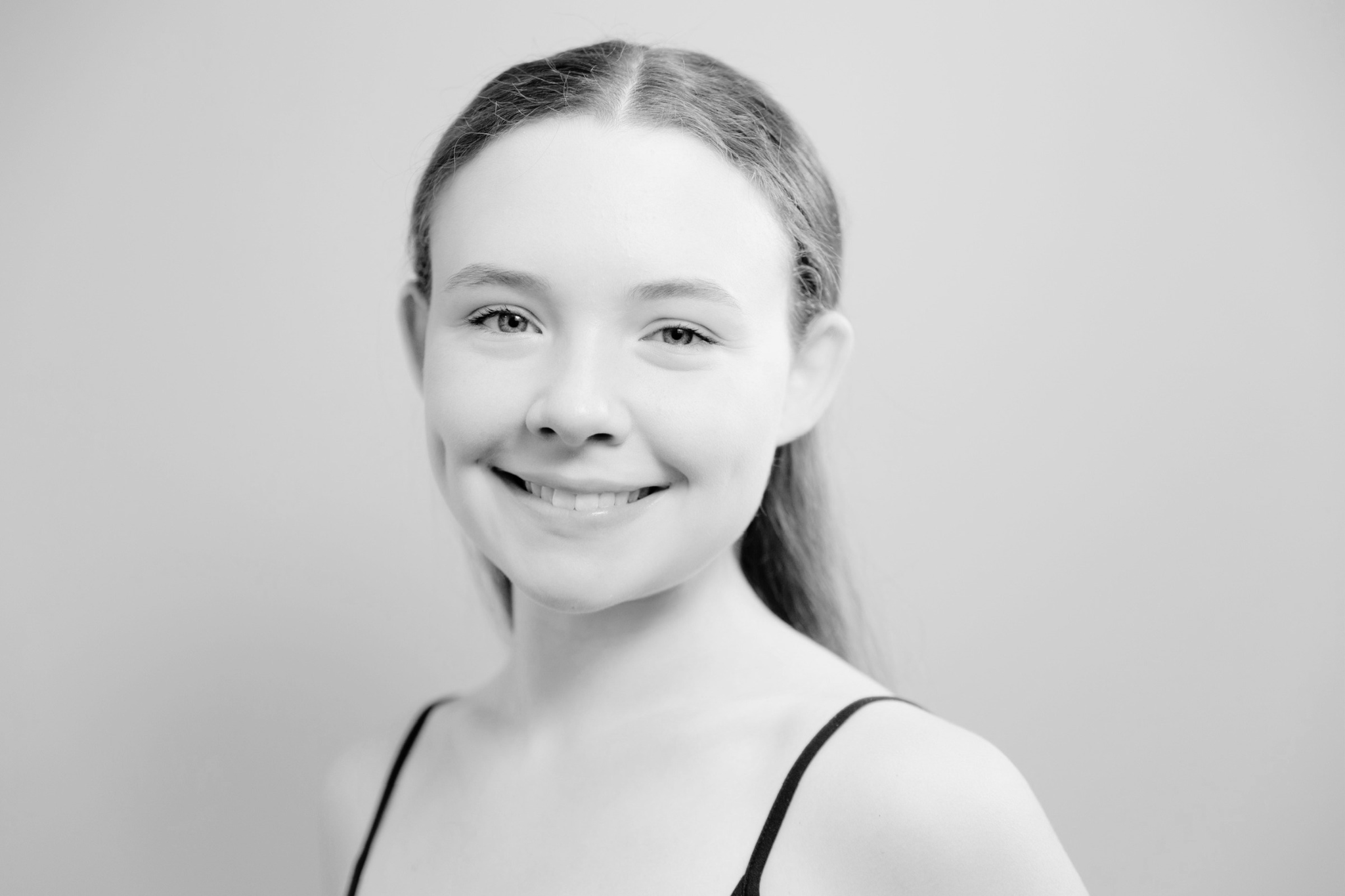 Black and white portrait of a young woman smiling, wearing a spaghetti strap top, with her hair pulled back.