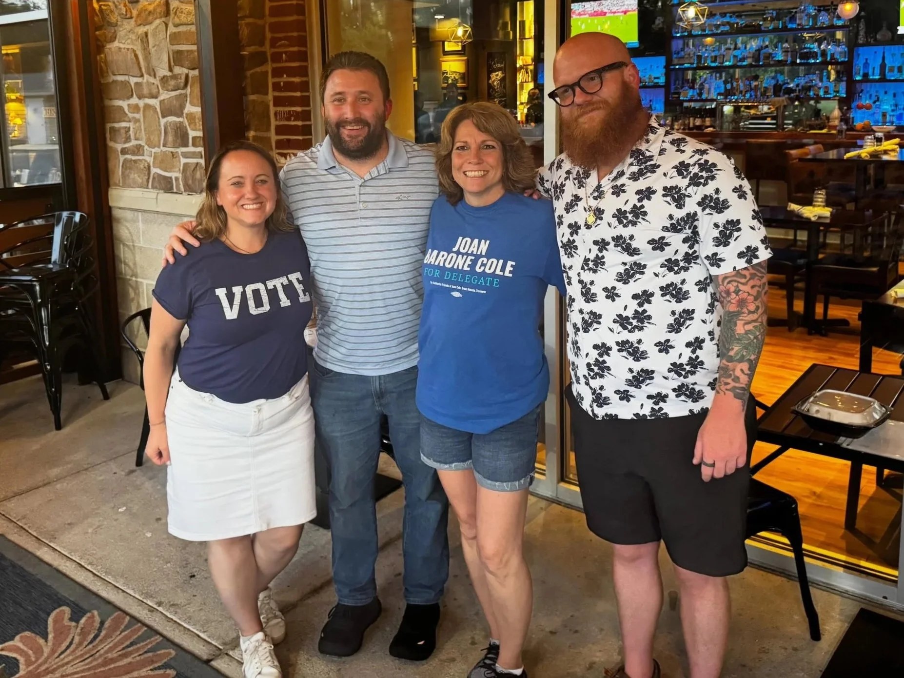 Four D31 candidates standing with arms around one another and smiling at the primary viewing party. The candidates are Heidi Schmidt, Brent Mulrooney, Joan Barone Cole, and Ryan Shaban.