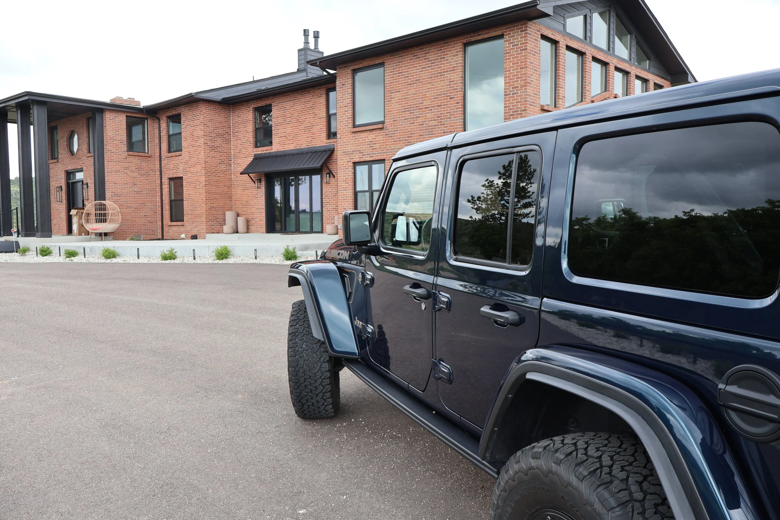 Black Jeep parked in front of a modern brick house with large windows and a small outdoor seating area.