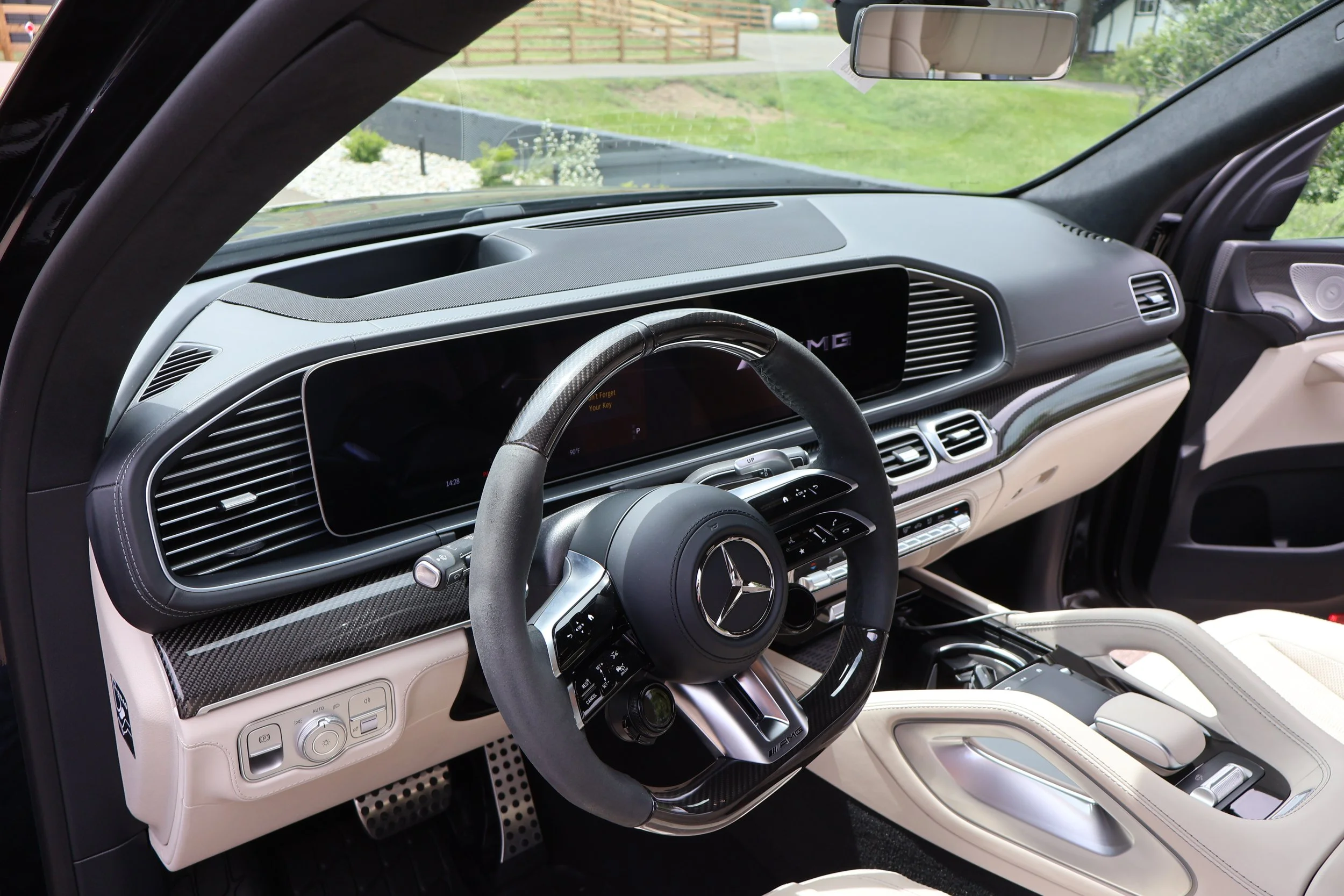 Interior of a luxury black Mercedes-Benz vehicle, showing the dashboard, steering wheel, and part of the center console, with a view outside through the windshield and side mirror.