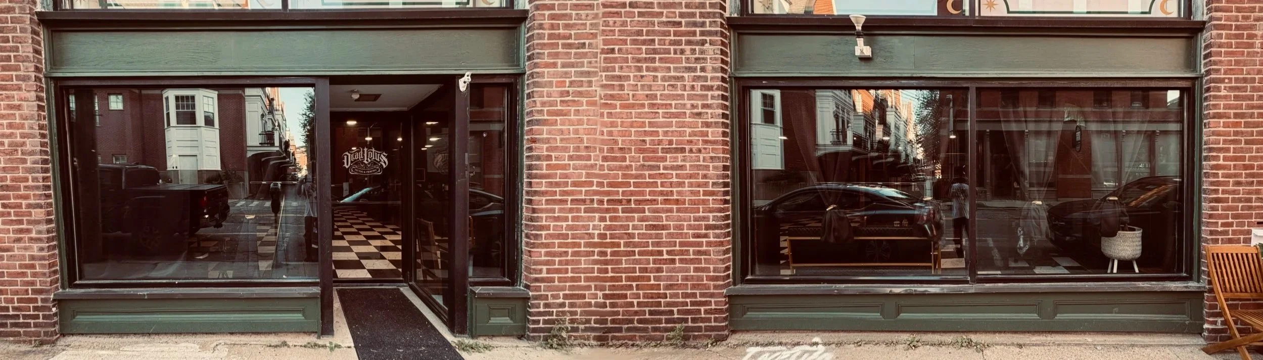 The exterior of a brick building with two large glass windows and an entrance door in the middle. Inside, a checkered floor, furniture, and a sign saying 'DeLuxe' are visible through the windows.