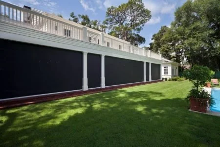 Side view of a backyard with a green lawn and a black wooden fence with white posts, trees and a blue sky in the background.