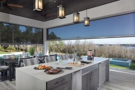 Modern kitchen with large island, window view of water and trees, hanging lights, and outdoor seating
