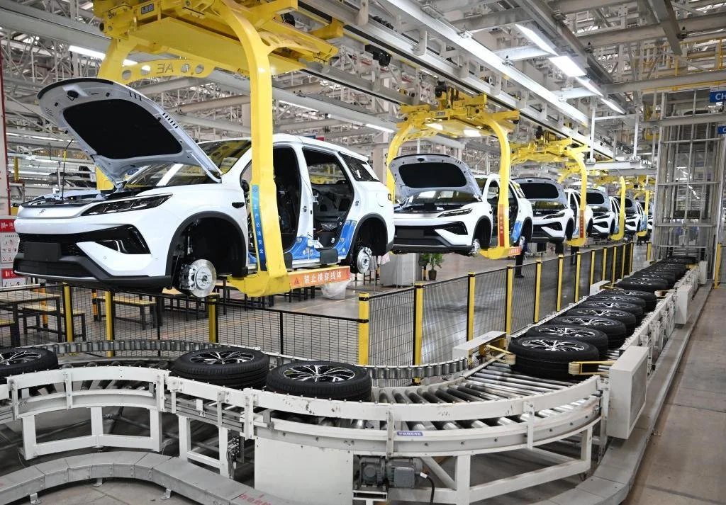 Automated assembly line with white electric SUVs in a factory, being assembled with wheels and components.