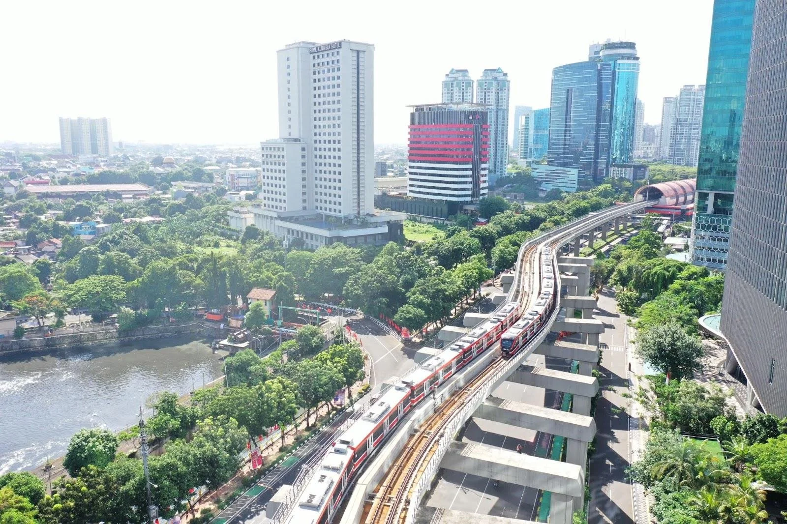 Cityscape with skyscrapers, trees, a river, and an elevated train running on tracks through the city.