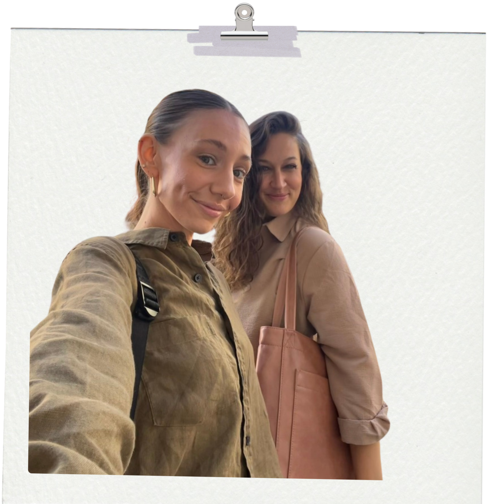 Co-Founders Paige Green and Elyse Schroeder smiling and taking a selfie, standing against a plain white wall, dressed in casual clothing, with one carrying a pink tote bag.