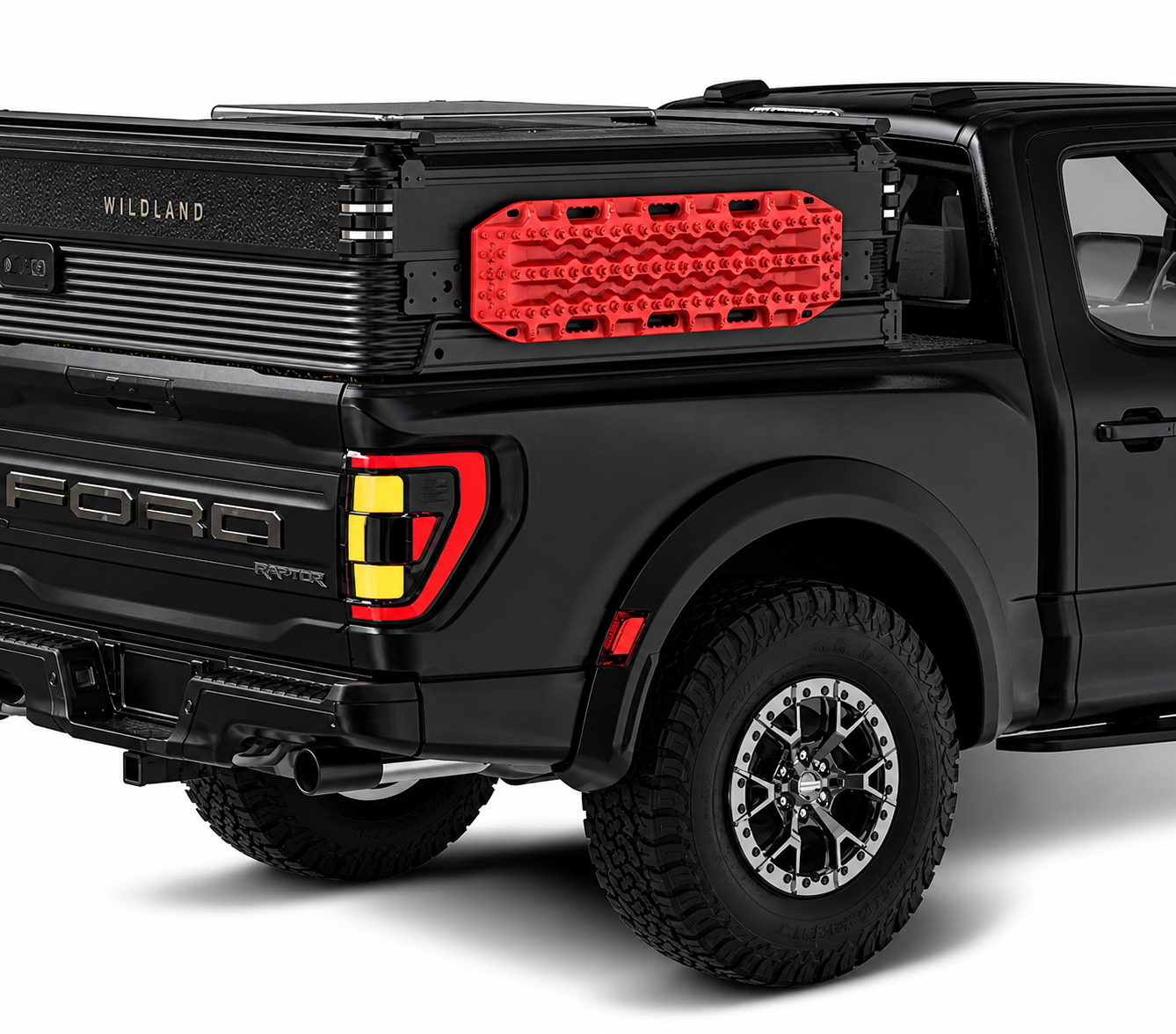 Black Ford F-150 Raptor pickup truck with a rugged off-road design, featuring a red traction board mounted on the truck bed, black alloy wheels, and tire tread visible.