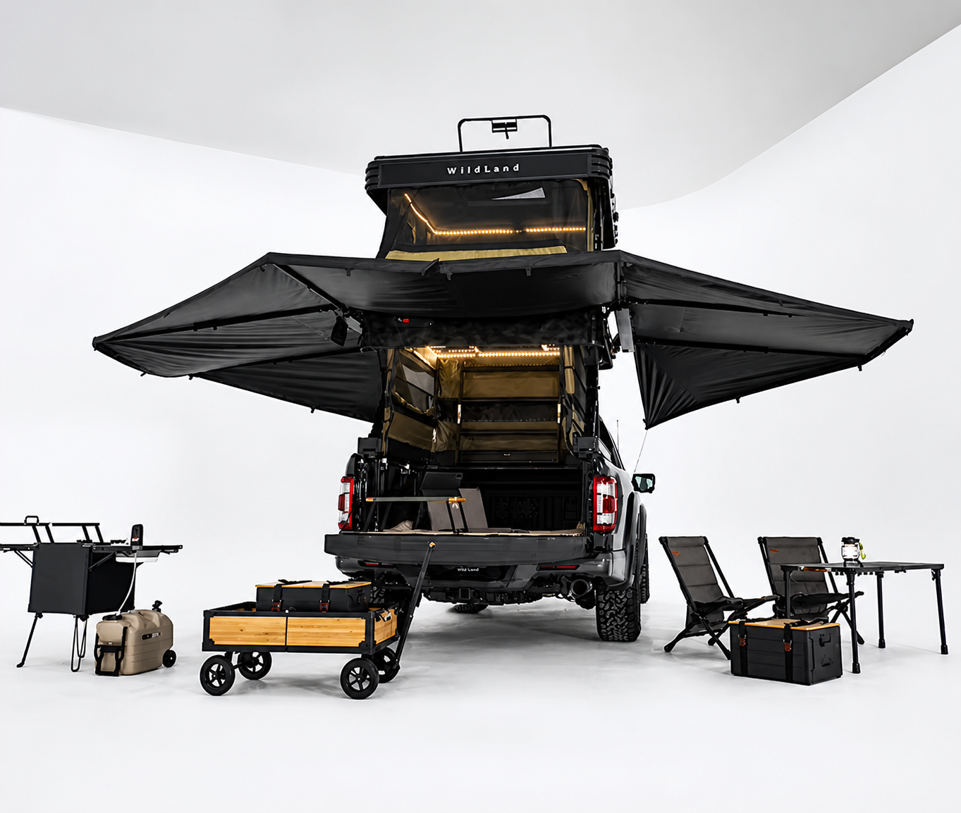 The image shows a black pickup truck with a pop-up camper mounted on its bed. The camper has extended black awnings on both sides. Surrounding the truck are camping and outdoor equipment, including a portable grill, a cooler, a rolling storage cart, camping chairs, a foldable table, and storage containers. The scene is set in a minimalist, well-lit studio with a plain white backdrop.