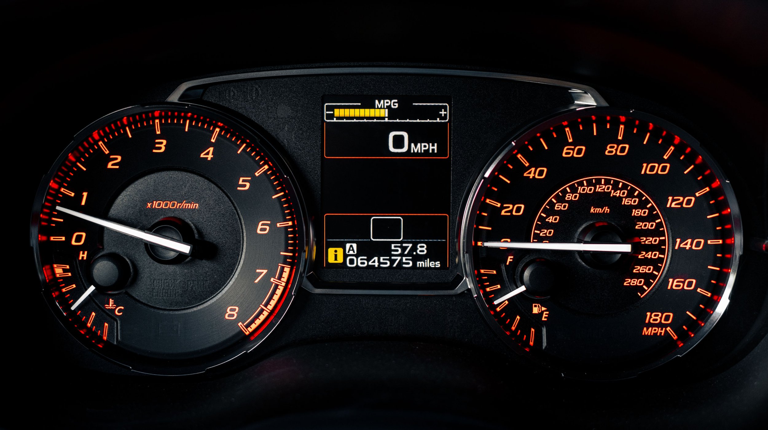 Close-up of a car dashboard showing speedometer, tachometer, and digital display with odometer and fuel gauge, all illuminated in red and white.