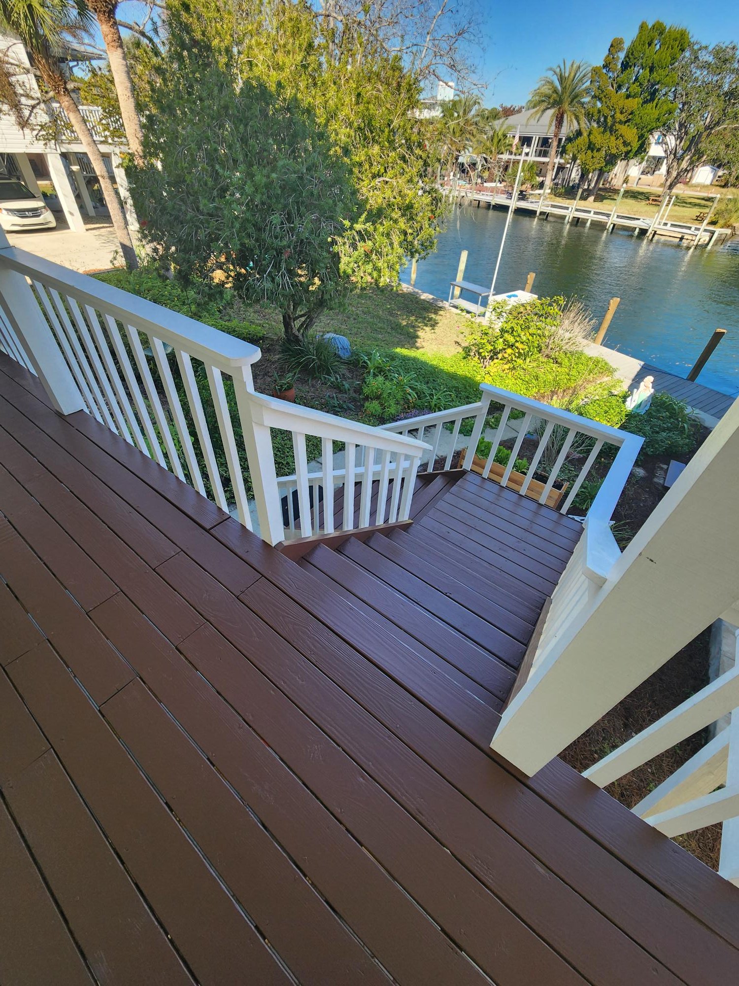 View from a balcony overlooking a garden and a canal with trees, houses, and docks in the background.