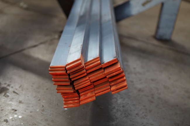 A bundle of metal square tubes with orange protective caps on the ends, resting on a workbench in a workshop.