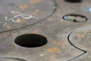Close-up of a metal workbench with several circular holes, showing rust and scratches.