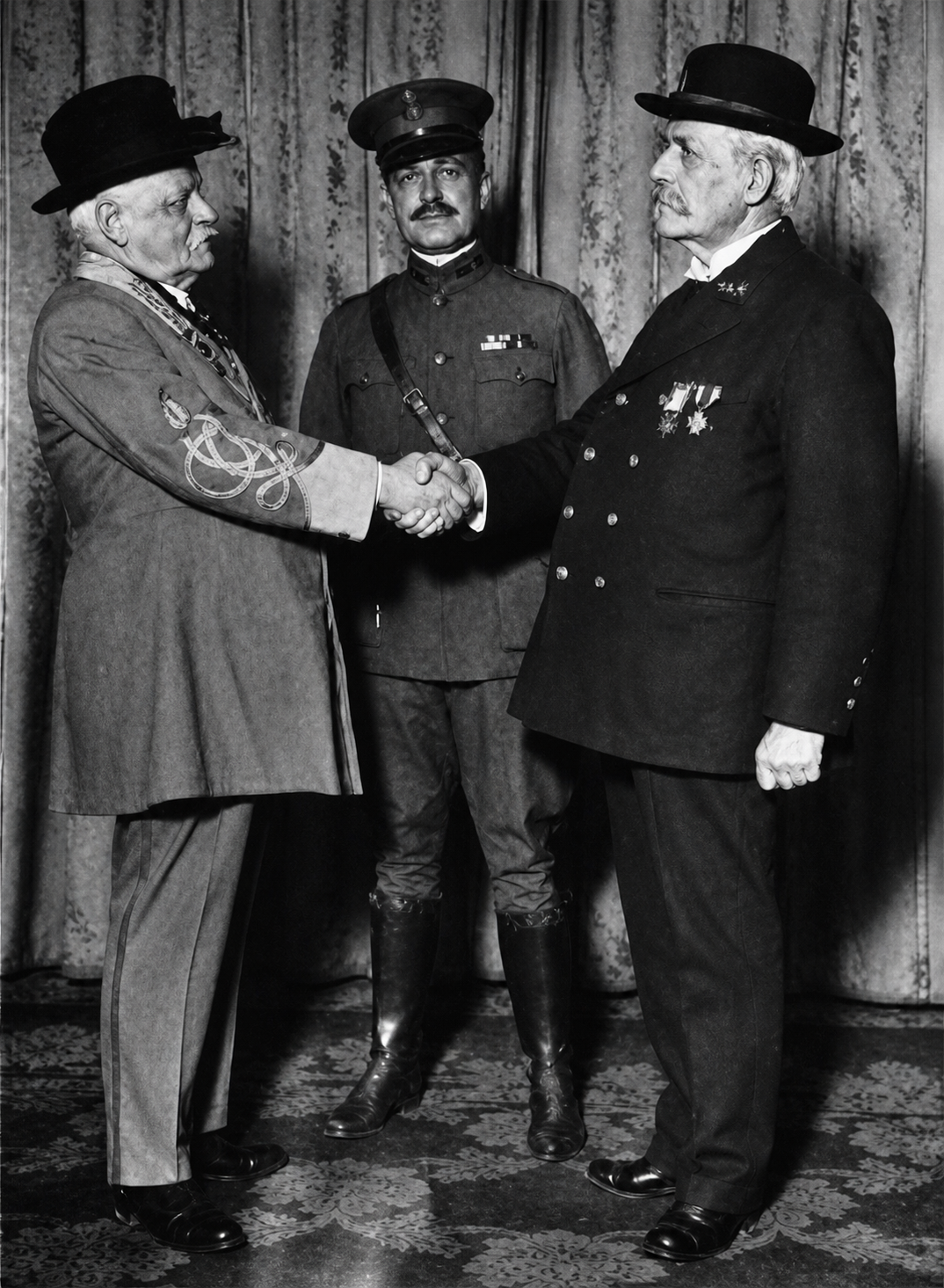 Two men in military and formal civilian attire shake hands, with a third man in uniform observing, in front of a curtain.