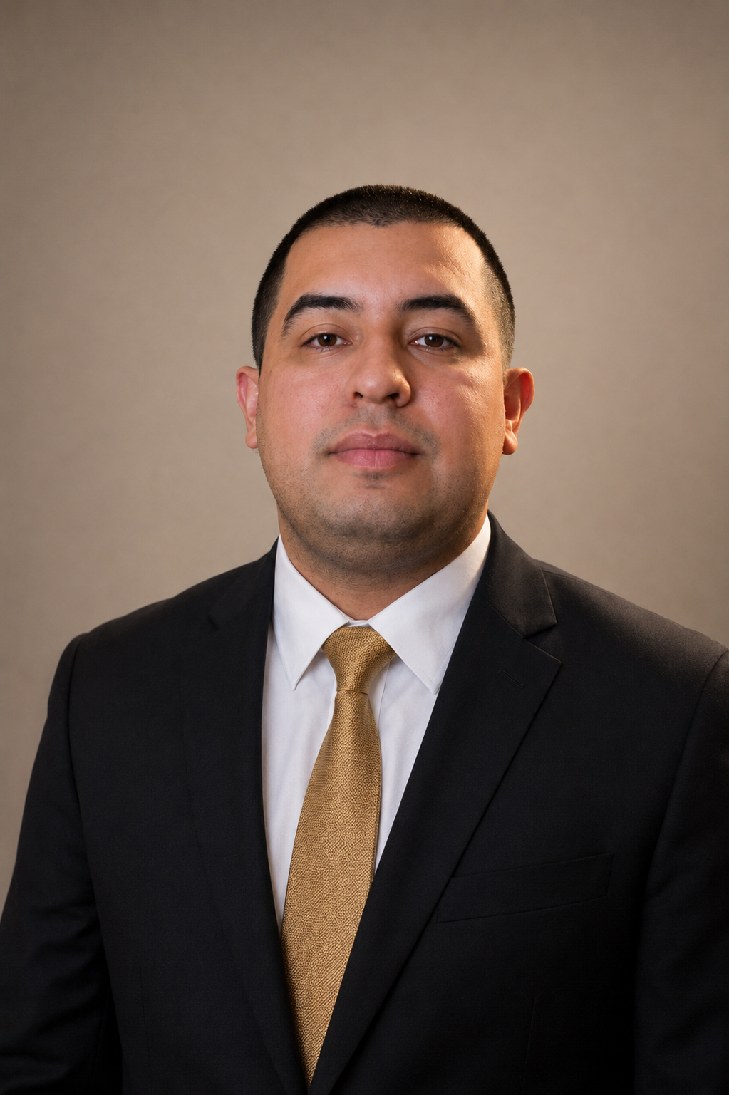 A professional headshot of a man wearing a black suit, white shirt, and gold tie, against a neutral background.