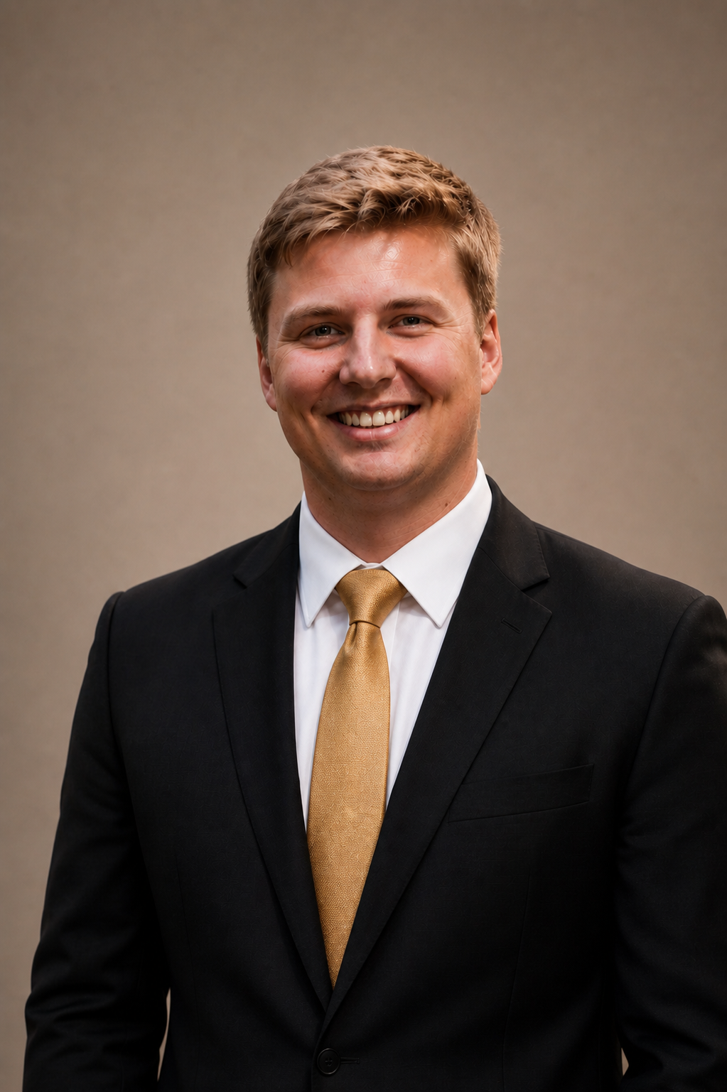 Photo of a young man smiling in a business suit with a white shirt and gold tie, against a plain background.
