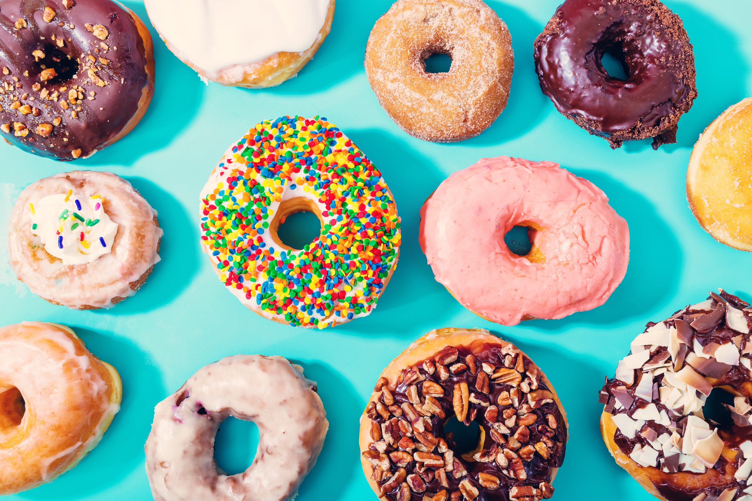 Assorted donuts with various icings and toppings on a turquoise background.