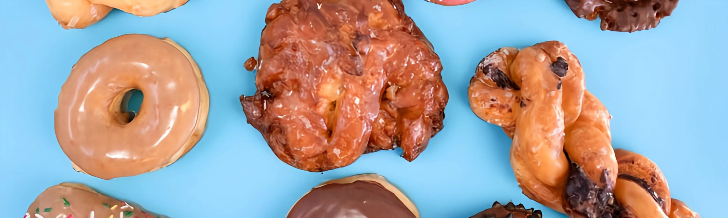 Assorted donuts with different toppings and glazes, placed on a light blue surface.