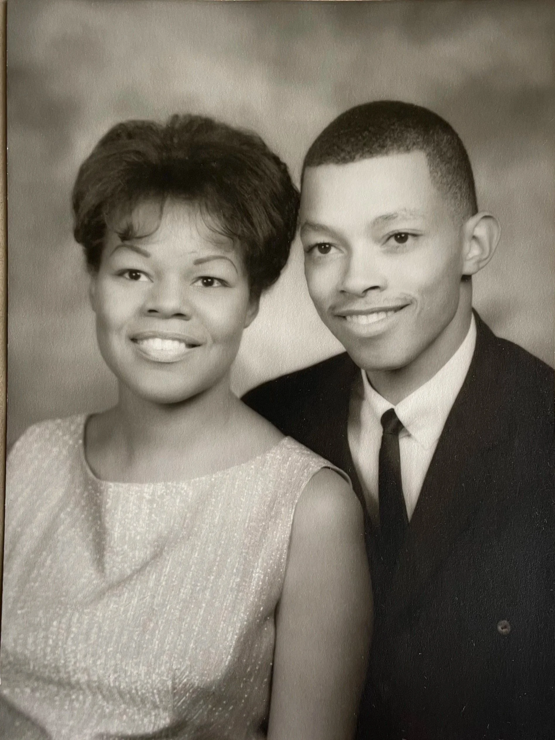 Sepia-toned headshot of Dorothy and Hurtis. Both are smiling and facing the camera. Dorothy is wearing a sleeveless top and Hurtis is wearing a black tuxedo jacket with a black tie. 