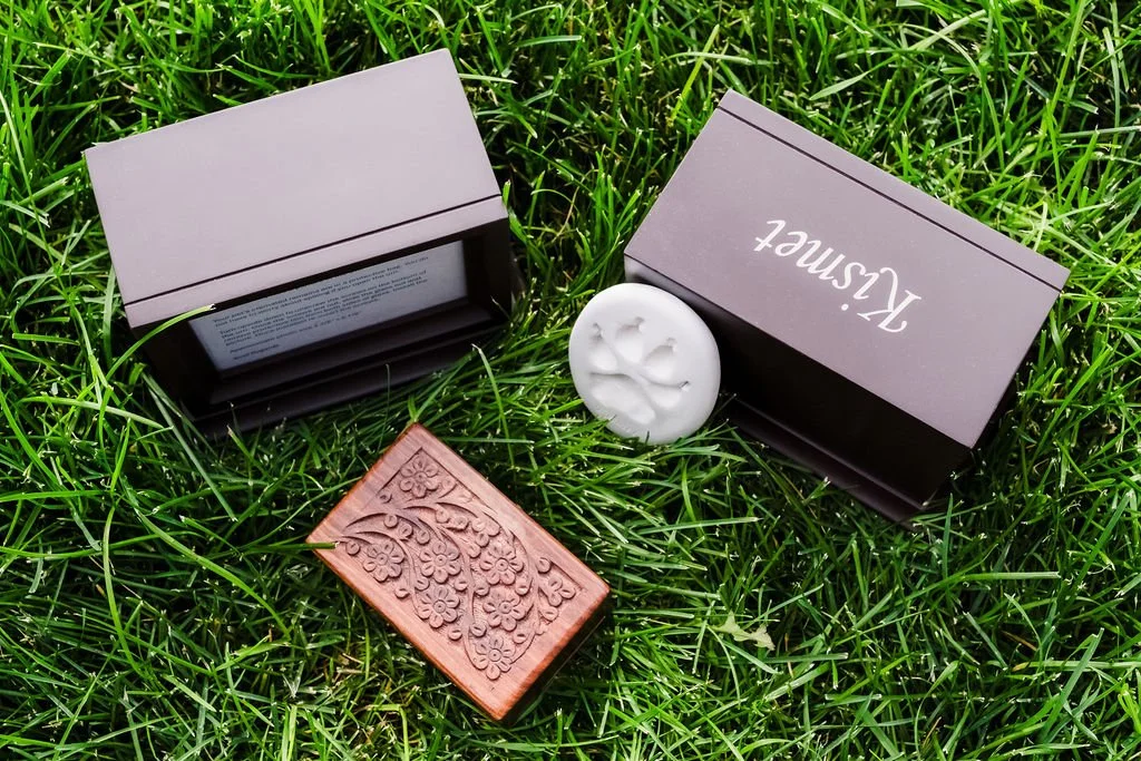 Two gray boxes, a carved wooden stamp, and a white candle on green grass.
