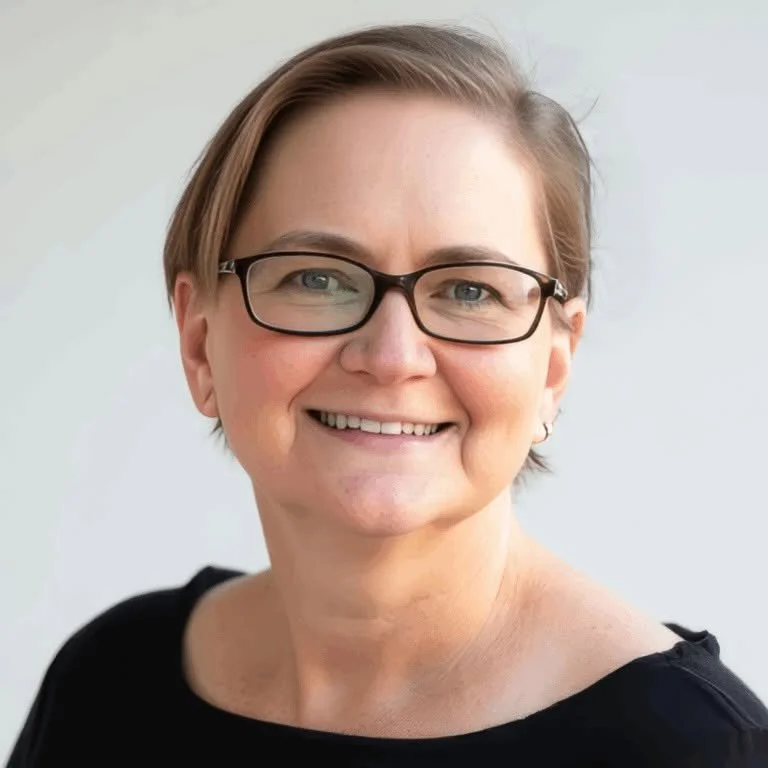 Close-up portrait of smiling woman with short hair, glasses, and black top against light background.
