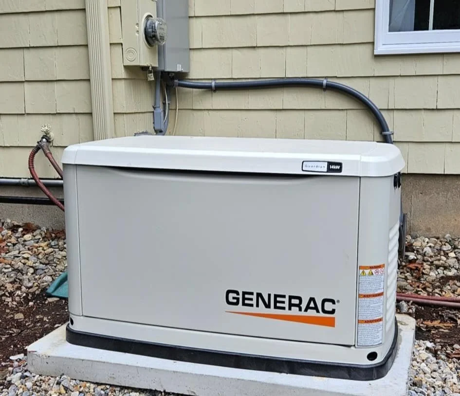A Generac home standby generator installed outside a house on a concrete pad, near a yellow house with siding and a window.