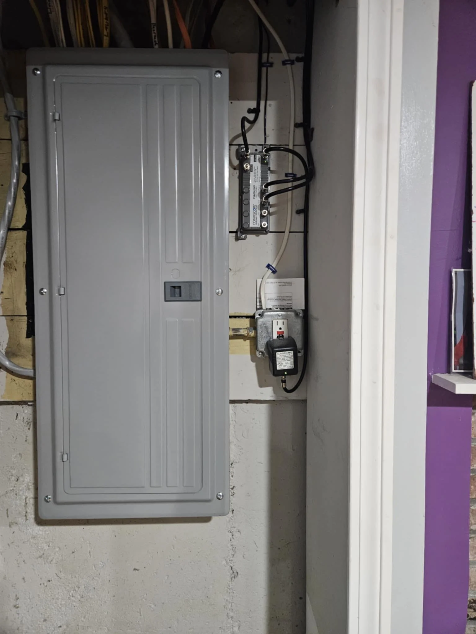 An electrical panel box on a wall with wiring and components inside, installed in a garage or utility room.