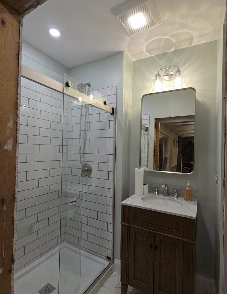 Bathroom with a glass shower enclosure, white subway tiles, a wooden vanity with a marble top, and a mirror above the sink.