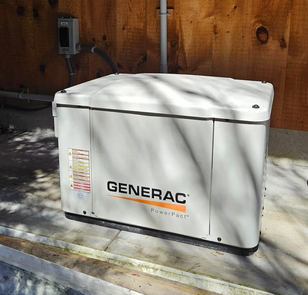 A white Generac PowerPact backup generator installed outside on a concrete pad next to a wooden wall.